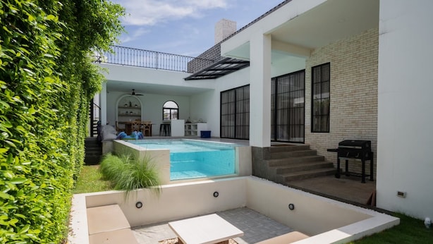 Un espace piscine extérieur moderne doté d’un coin salon couvert, d’un barbecue et d’un escalier menant à un niveau supérieur.