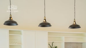 Une cuisine moderne avec des meubles blancs, un coin repas avec des chaises en bois et un canapé marron, ainsi que des luminaires suspendus.
