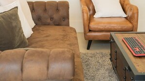 Une pièce comprenant un canapé en cuir marron, un fauteuil en cuir marron, une plante en pot et une table basse en bois sur laquelle se trouve un clavier.