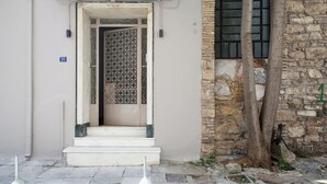 Una entrada de edificio con una puerta de metal, escalones que conducen a una puerta y un muro de piedra a la derecha.
