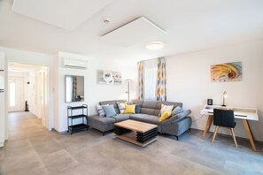 Un salon moderne avec un canapé d’angle gris, une table basse en bois et un bureau blanc avec une chaise.