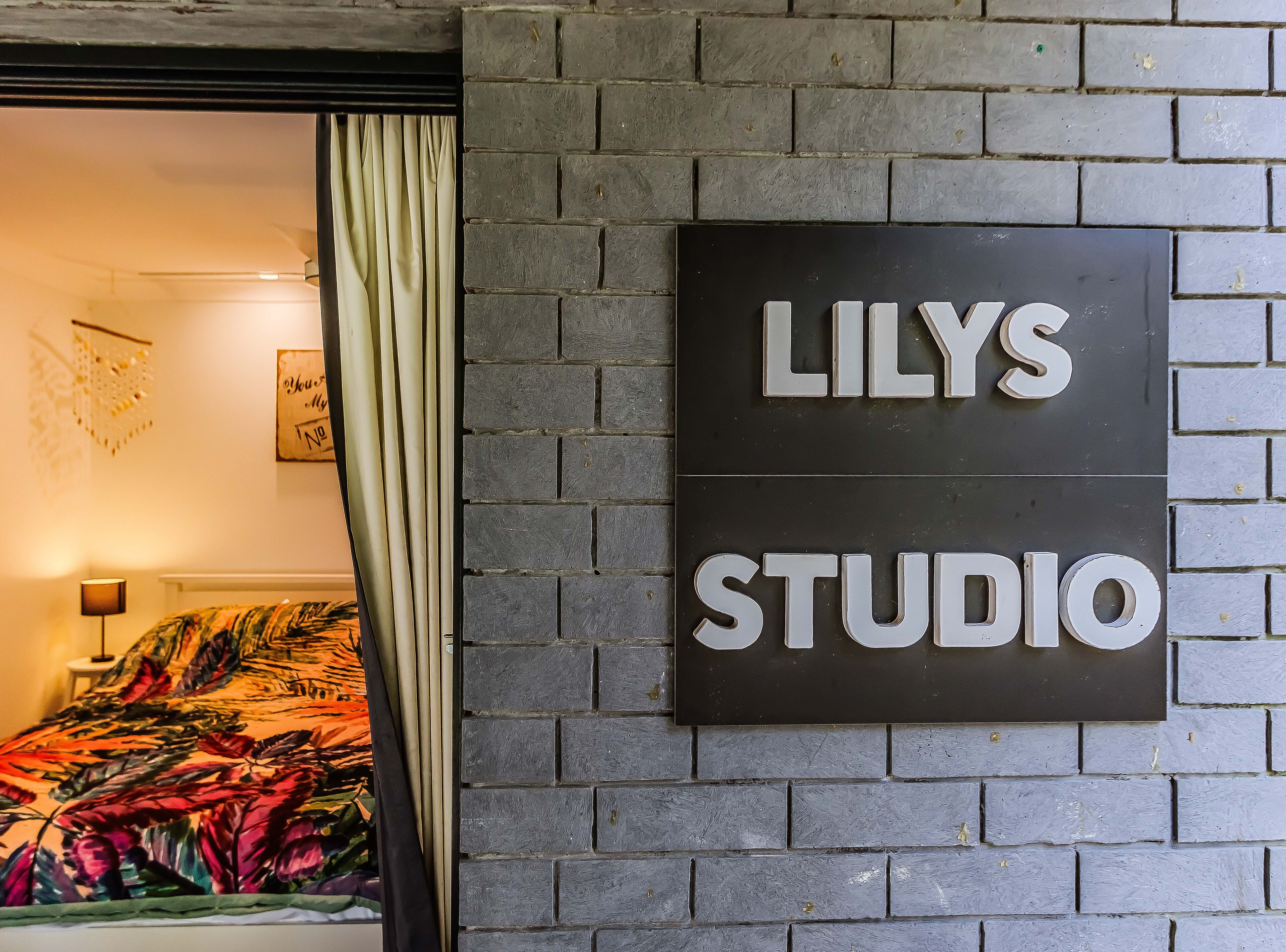Een bord met de tekst 'LILYS STUDIO' bevestigd aan een bakstenen muur.