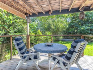 An outdoor patio with a round table and two chairs, surrounded by lush greenery. - Charming studio in the heart of Kingscliff! (Tweed)