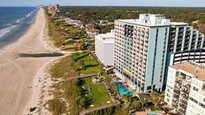 Un hôtel situé sur la côte, doté d’une grande piscine, offrant une vue sur la plage et comprenant plusieurs immeubles de grande hauteur.