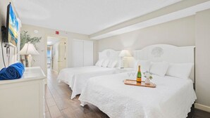 Une chambre d’hôtel avec deux lits, une télévision, une serviette bleue et un plateau avec une bouteille et des verres.