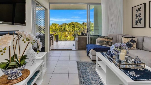 En moderne stue med sofa, sofabord og fjernsyn. Der er en balkon med udsigt til grønne områder.