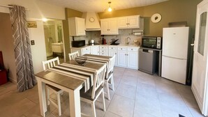 A compact kitchen with white cabinets, a dining table with chairs, a microwave, a toaster, and a refrigerator. - Charming cottage in Montbazon with terrace, garden, and parking (Montbazon)