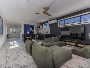 Uma sala de estar moderna com um conjunto de sofás, uma televisão de tela plana e um ventilador de teto.