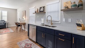 A modern kitchen with dark cabinets, a white countertop, and a stainless steel sink. - The Corner House (Huntsville)