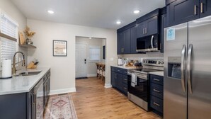 A modern kitchen with dark cabinets, stainless steel appliances, and a wooden floor. - The Corner House (Huntsville)