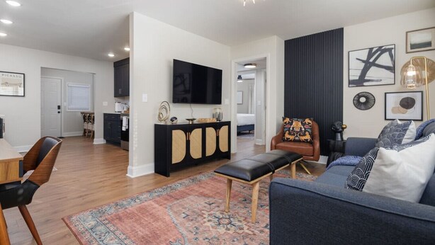 A modern living room with a sofa, a coffee table, a TV, and a dining area with a table and chairs. - The Corner House (Huntsville)
