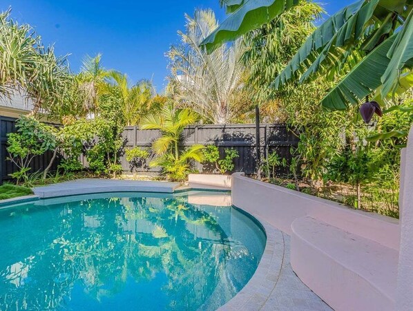 Uma piscina com borda curva, rodeada por vegetação tropical exuberante e um cercado de madeira.