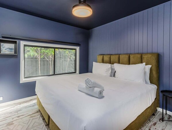 A bedroom with a large bed, a window, and a wall-mounted light fixture. - Welcome to your ultimate holiday getaway! (Tweed)