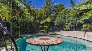 A swimming pool with a tiled table and chairs, surrounded by lush greenery. - Welcome to your ultimate holiday getaway! (Tweed)