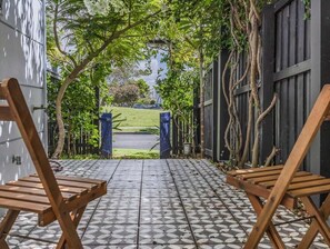 Een terras met patroontegels, twee houten stoelen en uitzicht op een groen gazon en bomen.