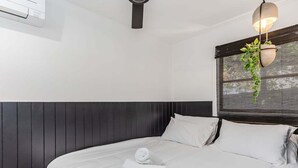 Hotellihuone, jossa on suuri sänky, ruukussa oleva kasvi, riippuvalaisin ja ikkuna, jossa on sälekaihtimet.