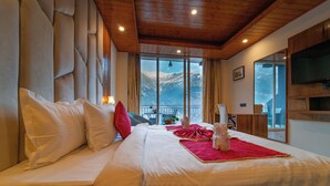 Una cama grande con sábanas blancas, una manta roja y vistas de la montaña a través de amplias ventanas.