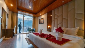 Habitación de hotel con una cama grande, techo de madera, vistas a montañas y un balcón.