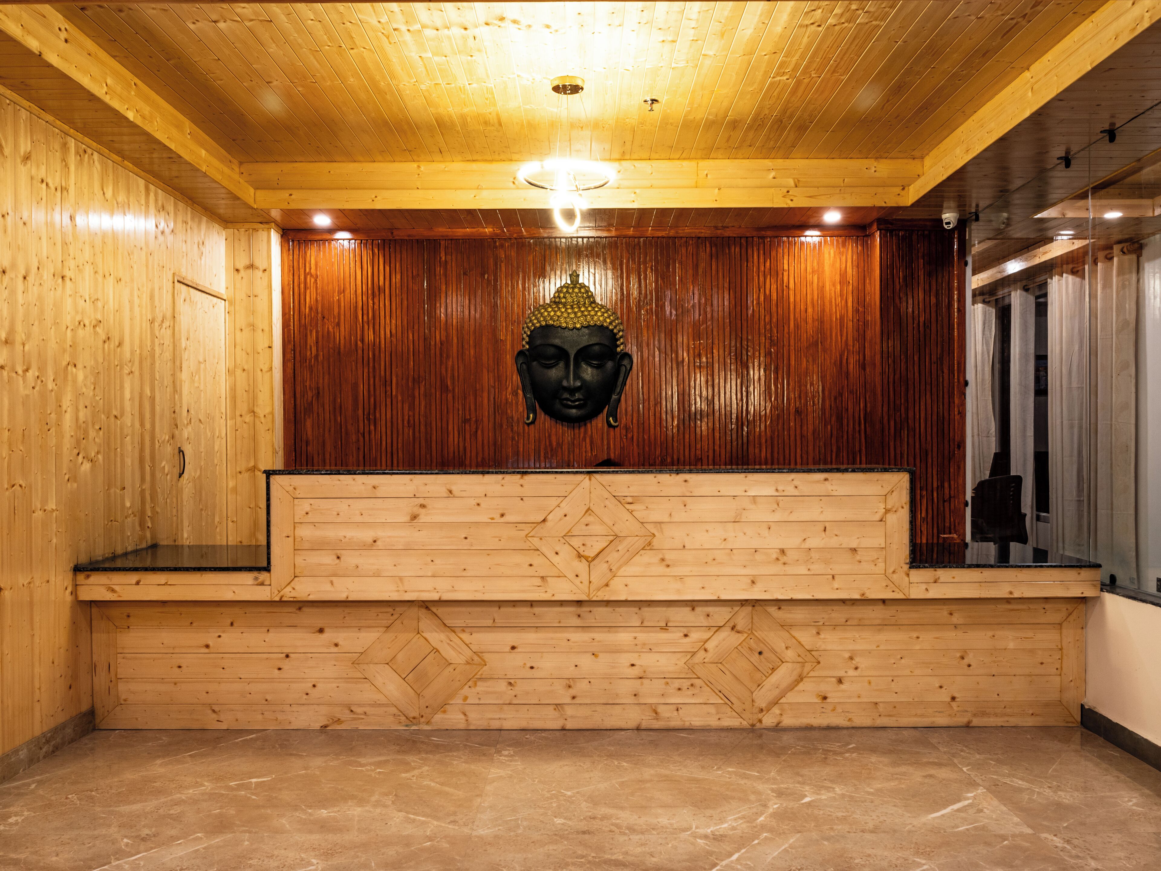 A wooden reception desk with a Buddha head sculpture above it, a tiled floor, and wooden panel walls.
