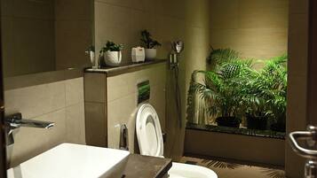 A modern bathroom with a sink, toilet, and shower. There are plants on the shelves and a mirror above the sink.