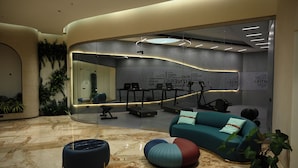A modern lobby with a curved seating area, a fitness center visible through a glass wall, and a marble floor. - 0484 Aero Lounge - Terminal 2, Cochin Airport Hotel (Aluva)