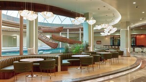 A modern hotel lobby with a central pool, seating areas, and a staircase leading to upper levels. - 0484 Aero Lounge - Terminal 2, Cochin Airport Hotel (Aluva)