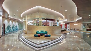 A spacious lobby with a curved ceiling, a seating area with colorful ottomans, and a mural of tropical leaves on the wall. - 0484 Aero Lounge - Terminal 2, Cochin Airport Hotel (Aluva)