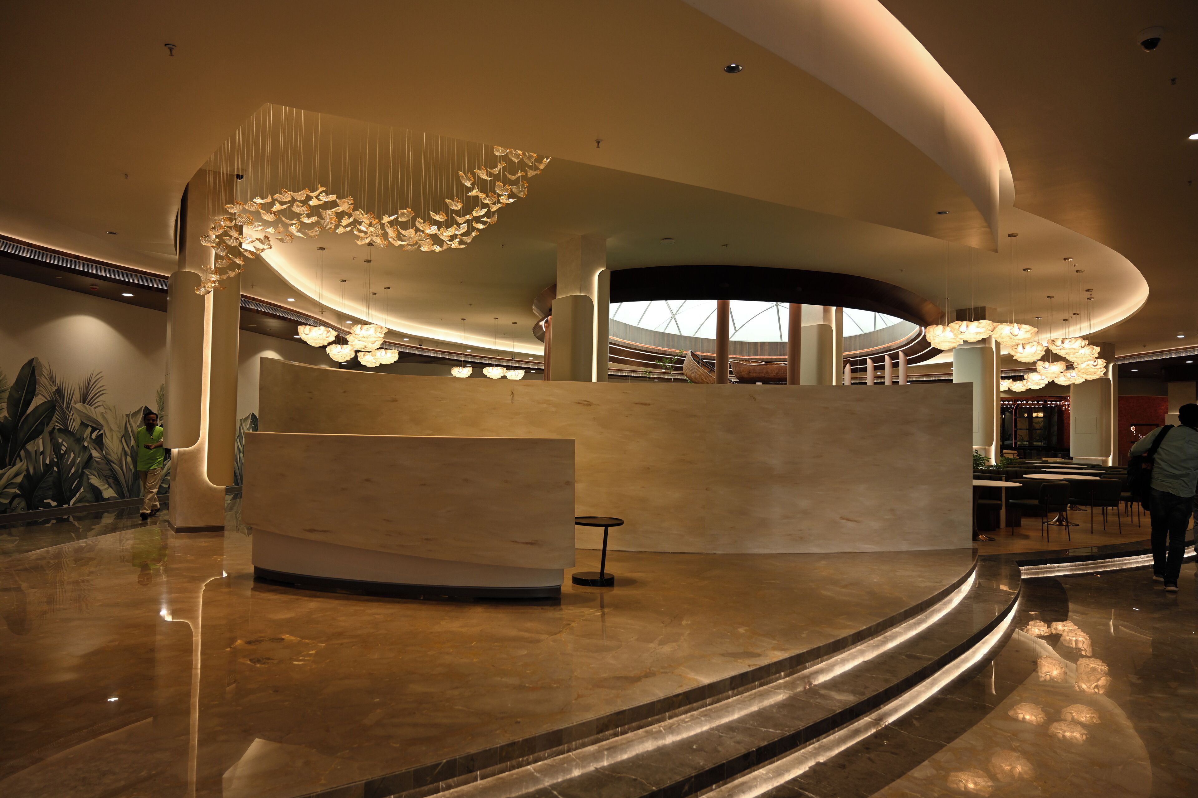 A modern lobby with a curved reception desk, large hanging light fixtures, and a spacious area with a polished floor.
