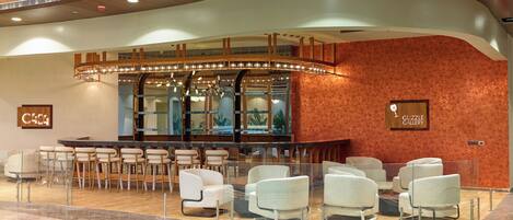 Un hall con techo curvo, una zona de bar con asientos y un letrero en la pared que dice 'GUZZLE GALLERY'.