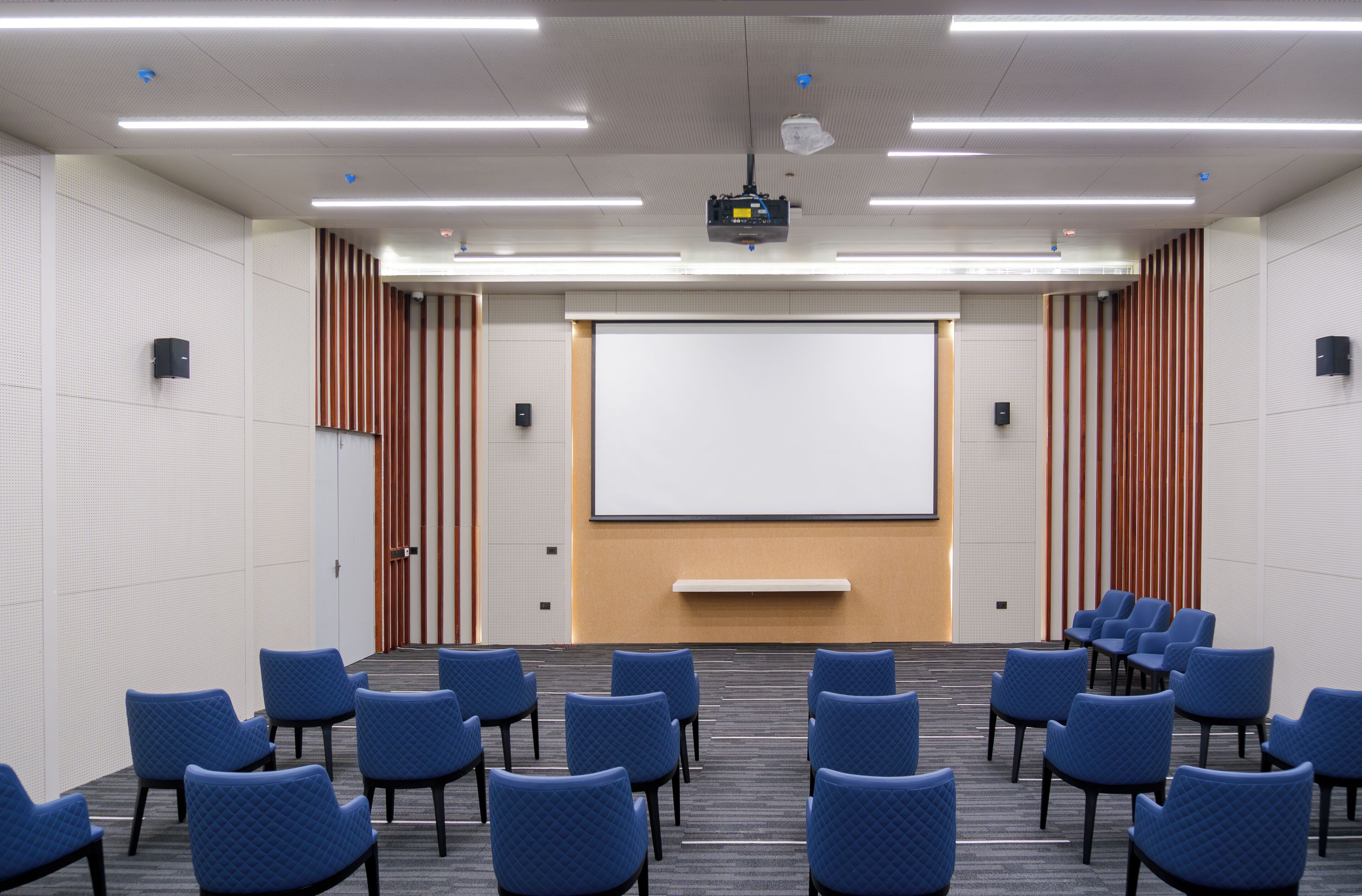 A conference room with rows of blue chairs, a large projection screen, and a whiteboard.
