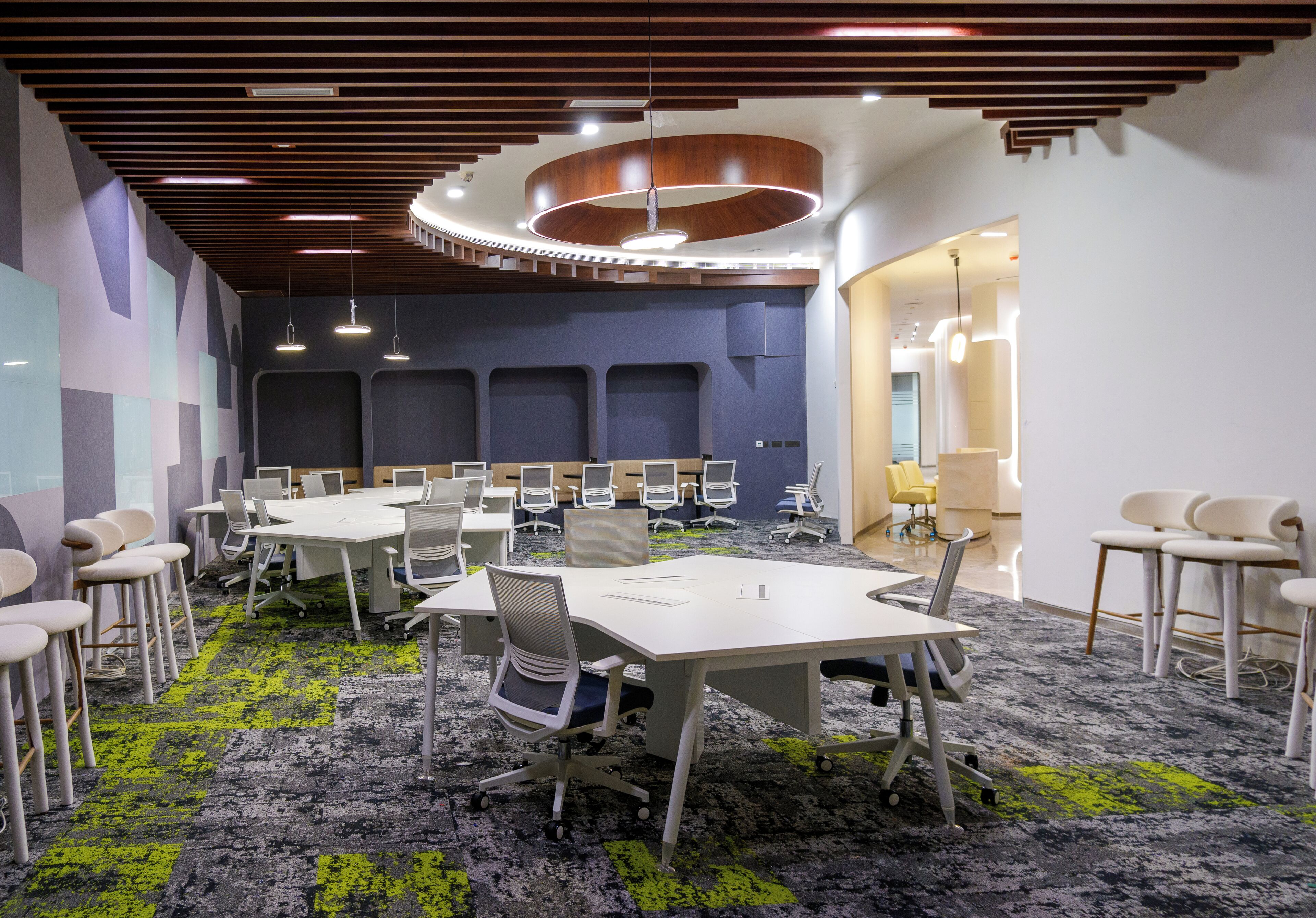 Une salle de conférence dotée de plusieurs tables et chaises, d’un sol recouvert de moquette et d’un plafond au design moderne.