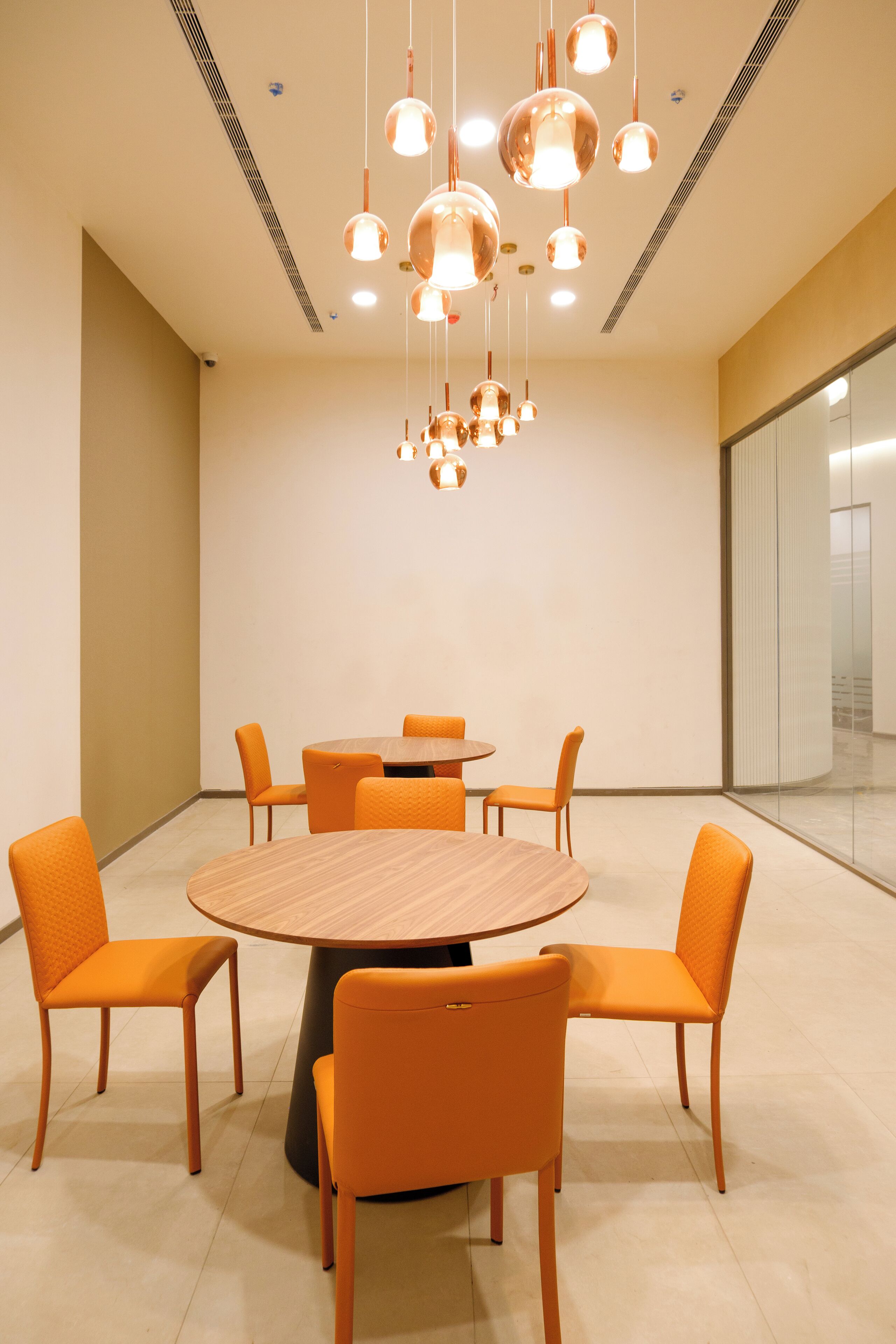 A conference room with a round wooden table, six orange chairs, and a modern chandelier.