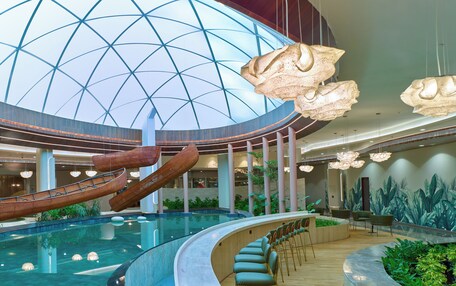 A spacious indoor area with a large pool, seating areas, and a high ceiling with a geometric glass design.