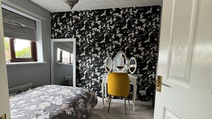 Ein Schlafzimmer mit Bett, Schreibtisch, Stuhl, Spiegel und einer Tür.