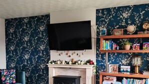 Ein gemütliches Wohnzimmer mit Kamin, einem an der Wand befestigten Fernseher und einem Bücherregal voller Bücher und Dekoration.