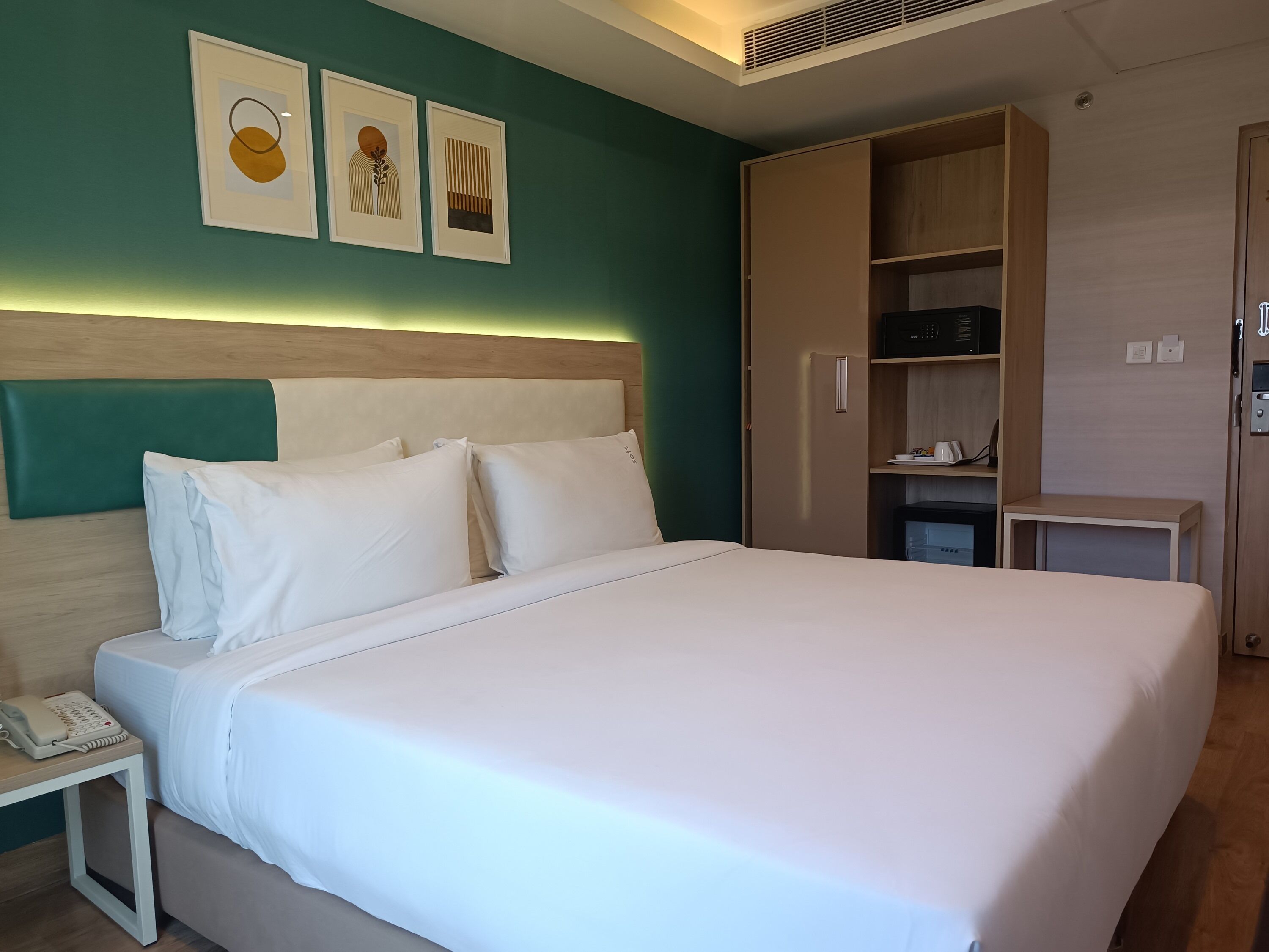 Una cama bien hecha con sábanas blancas, un teléfono en la mesita de noche y un cabecero con detalles en color turquesa.
