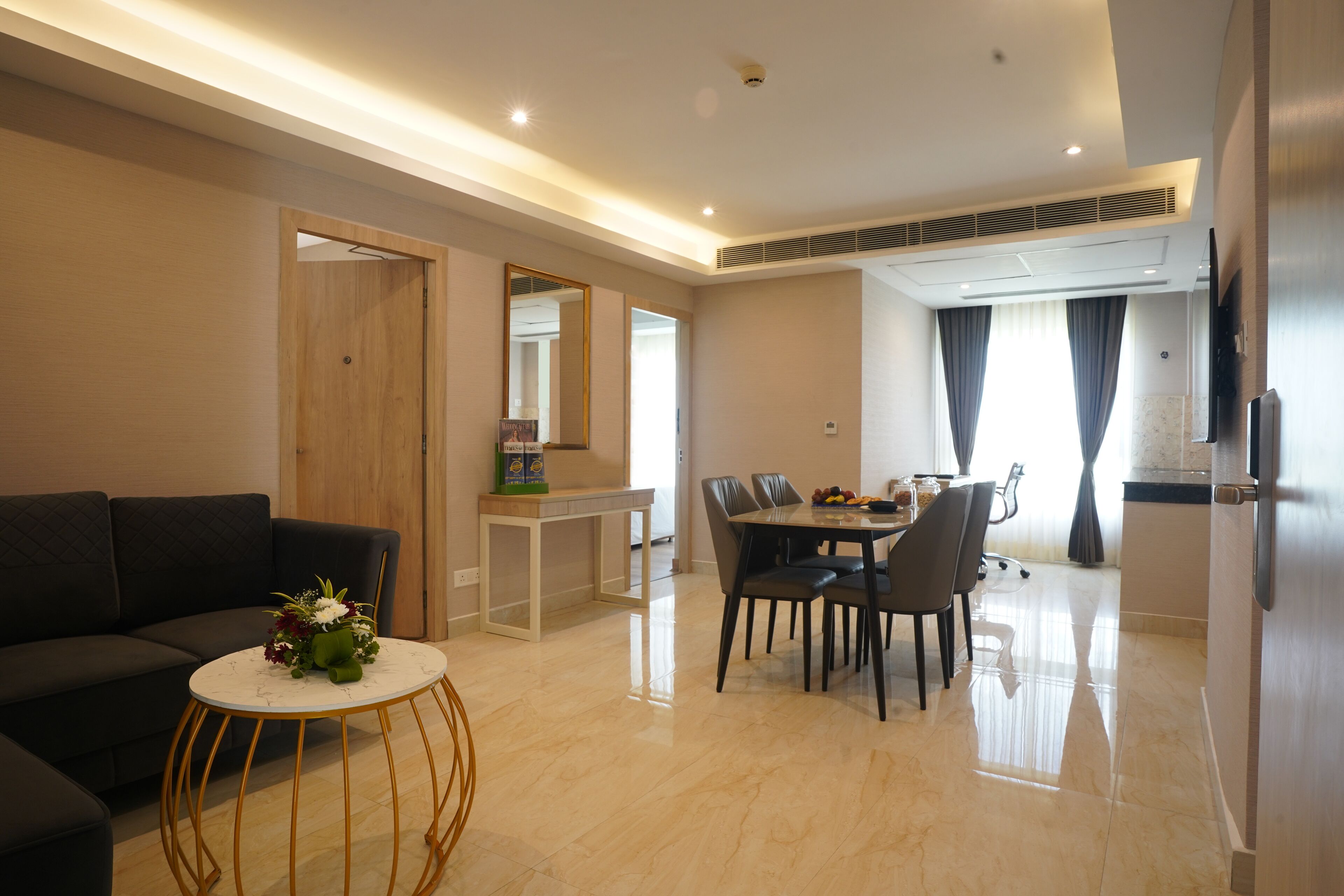 A modern living room with a sofa, a round coffee table, a dining table with chairs, a TV, and a kitchen area with a refrigerator.