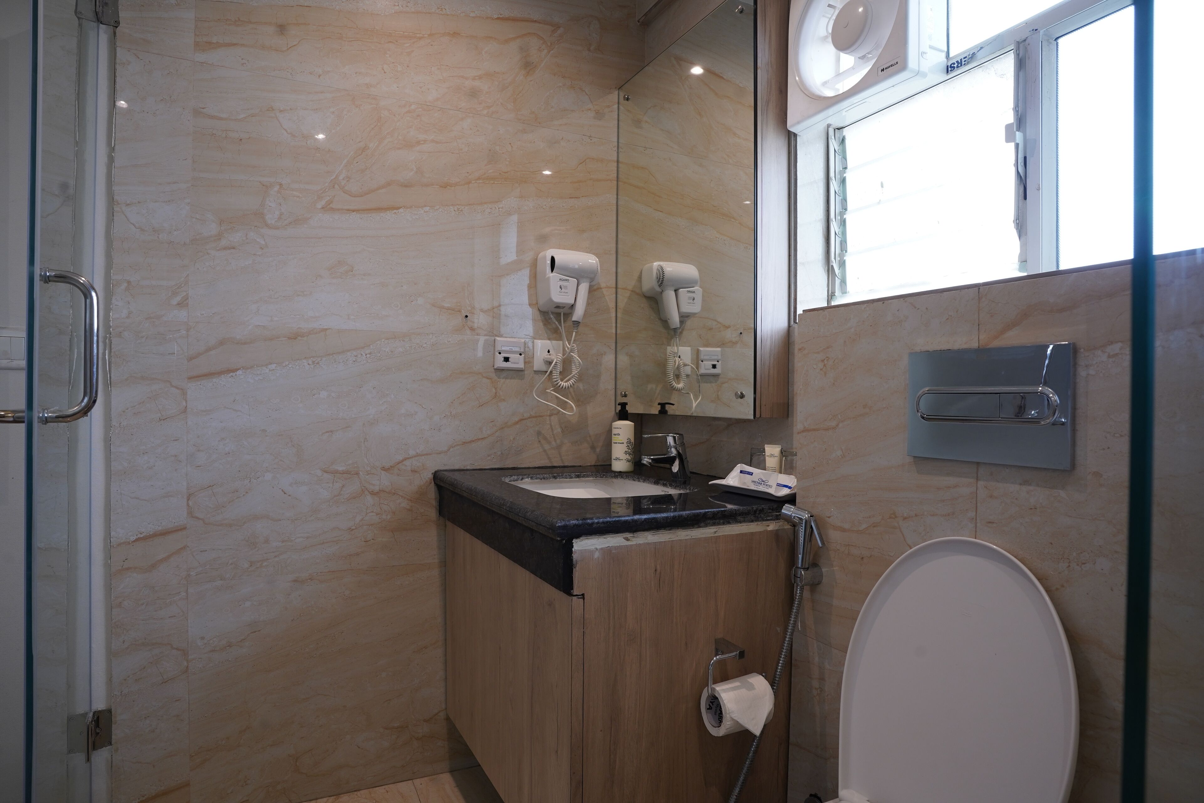 Un baño moderno con pared de mármol, lavamanos, inodoro y cabina de ducha de vidrio.