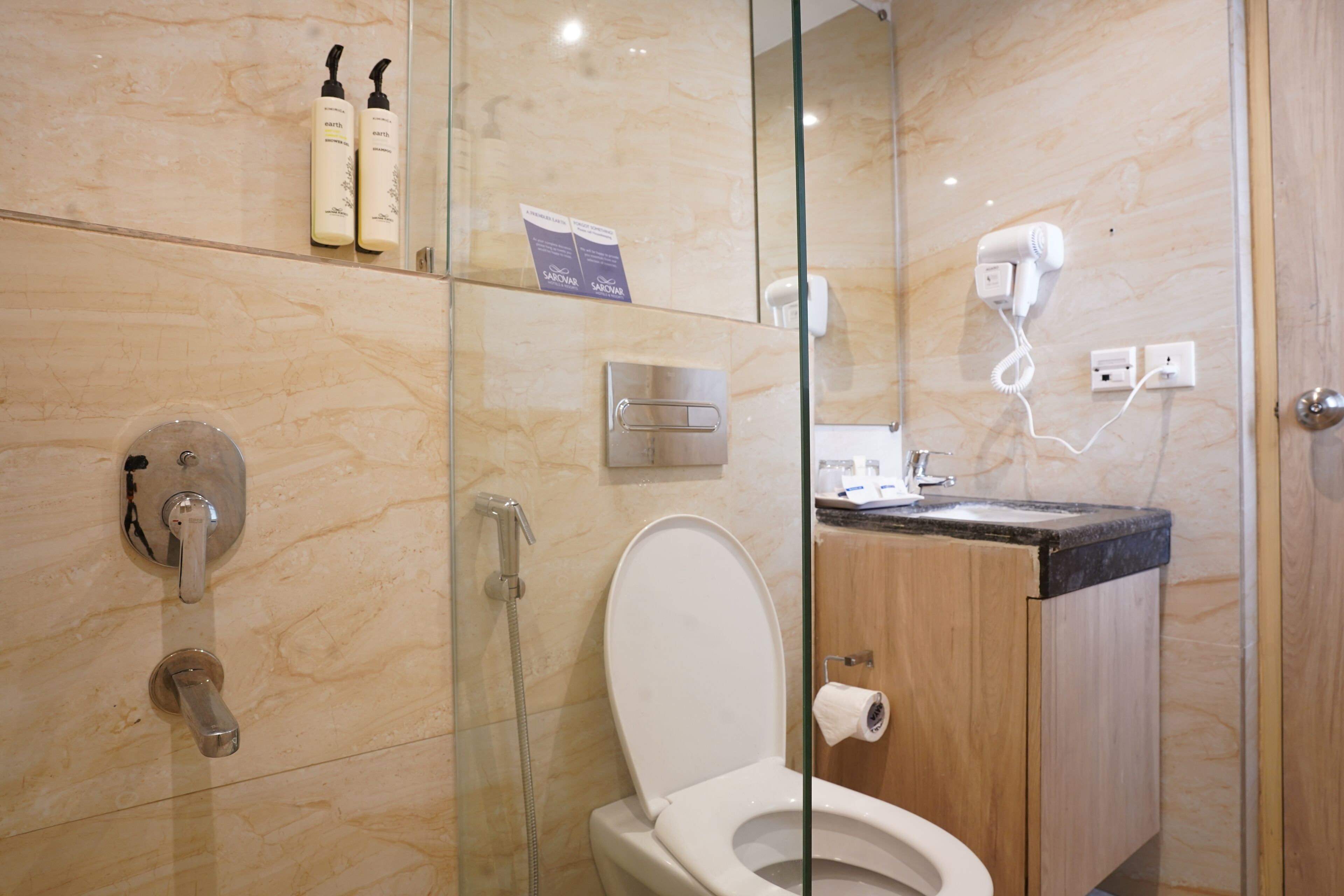 A modern bathroom with a glass-enclosed shower, a toilet, and a sink with a hairdryer.