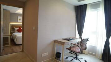 A hotel room with a bed, a desk with a chair, a window with curtains, and a mirror reflecting the room.