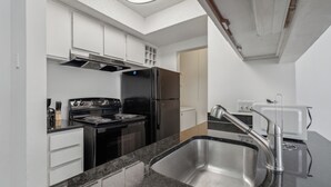 Una cocina moderna con un lavamanos de acero inoxidable, una estufa negra y armarios blancos.