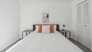 Un dormitorio con cama, dos mesitas de noche, un tocador, lámpara, armario y un cuadro en la pared.