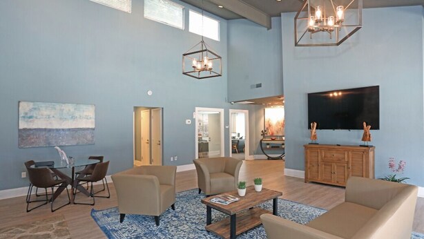 A spacious living room with a high ceiling, a large TV, and a dining area with a glass table and chairs. - Northcliffe 404 I Fully Furnished 1 Bedroom 1 Ba (Winston-Salem)