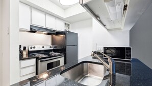 A modern kitchen with white cabinets, a stainless steel sink, a black countertop, a stove, a microwave, and a ventilation hood. - Northcliffe 404 I Fully Furnished 1 Bedroom 1 Ba (Winston-Salem)