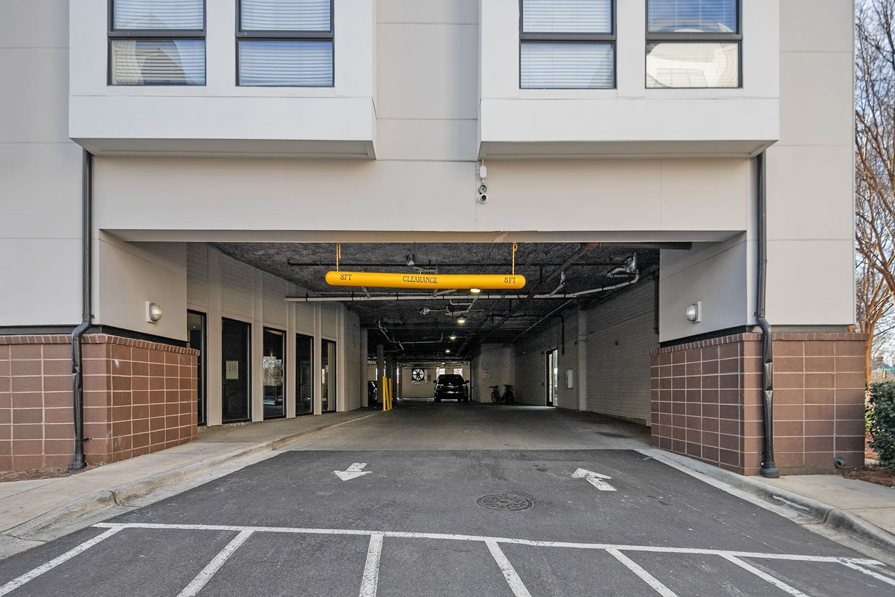 A parking garage entrance with clear directional arrows on the ground, a yellow clearance sign overhead, and a vehicle parked inside.