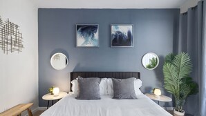 A modern bedroom with a large bed, two bedside tables, a round mirror, and two framed artworks on the wall. - Spacious 2BD With Private Balcony and Free Parking 2 (Charlotte)