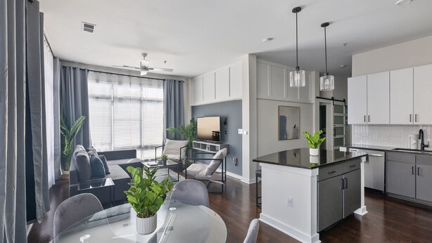 A modern kitchen with white cabinets, a dining area with a glass table, and a living room with a sofa and chairs. - Spacious 2BD With Private Balcony and Free Parking 2 (Charlotte)