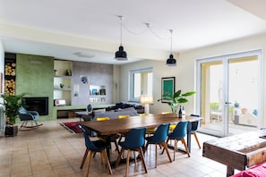 A spacious living area with a wooden dining table, blue chairs, a fireplace, and a large window.