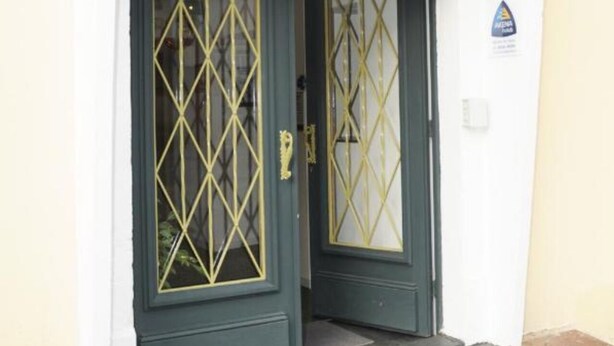 Ein Hotel Eingang mit einer dunkelgrünen Tür, verziert mit einem geometrischen Muster, und einem goldfarbenen Schild darüber, auf dem 'HOTEL' steht.