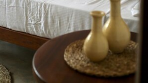 A bed with white bedding and two decorative pillows, a woven mat with two vases, and a wooden headboard. - Room in Chalet - Amlou Surf House - Villa (Mirissa)